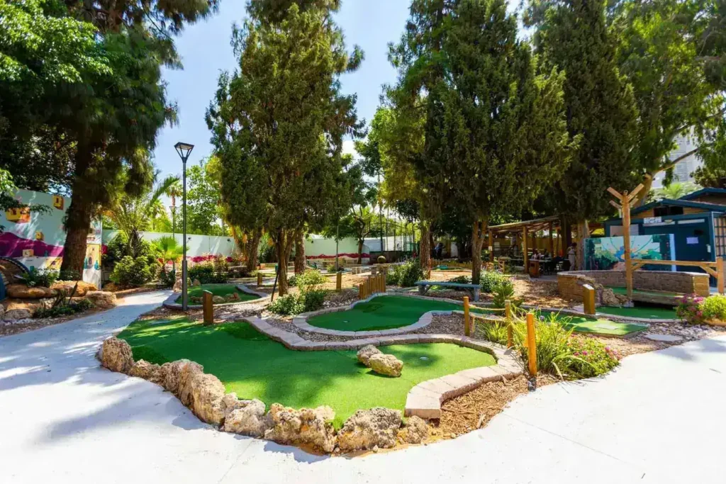 מגרש מיני גולף מטופח, מוקף בצמחייה, מתאים לפעילות משפחתית מגבשת או רעיון לדייט.