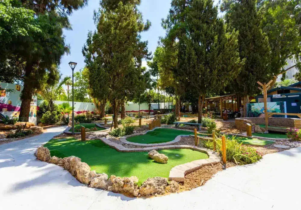 מגרש מיני גולף מטופח, מוקף בצמחייה, מתאים לפעילות משפחתית מגבשת או רעיון לדייט.